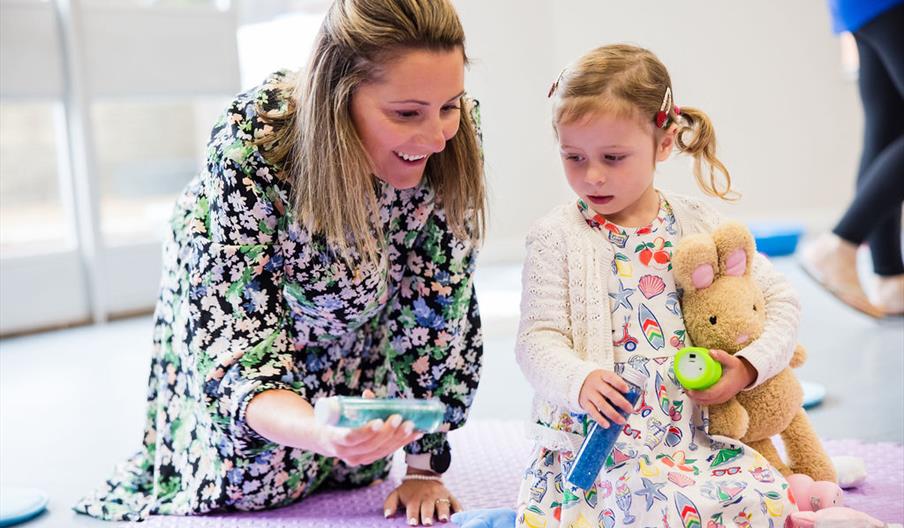 A mum and pre-schooler playing on a mat in the class with some sensory toys