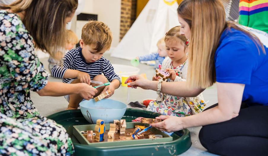 The class leader and a parent playing with some preschoolers at a messy play tray