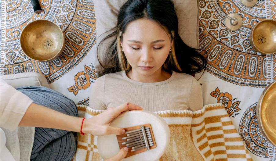 Woman resting during a sound bath surrounded by singing bowls and sound healing instruments.