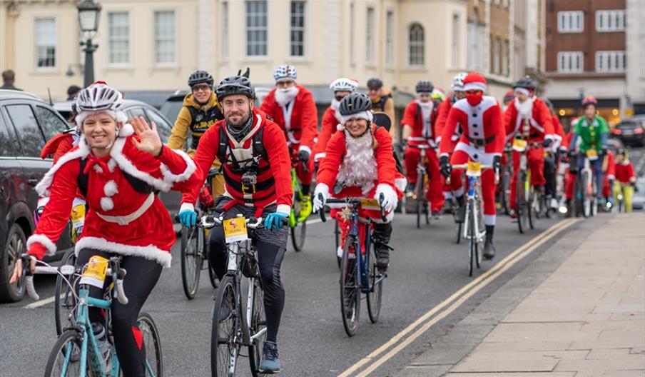 A cycling santa smiling and waving with other cycling Santas behind her