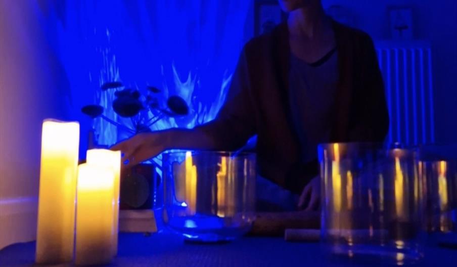Lady sitting in front of blue lights and 3 crystal bowls, playing the therapeutic instruments