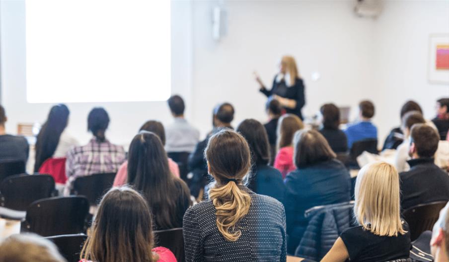 A lecture hall with people facing towards a screen.