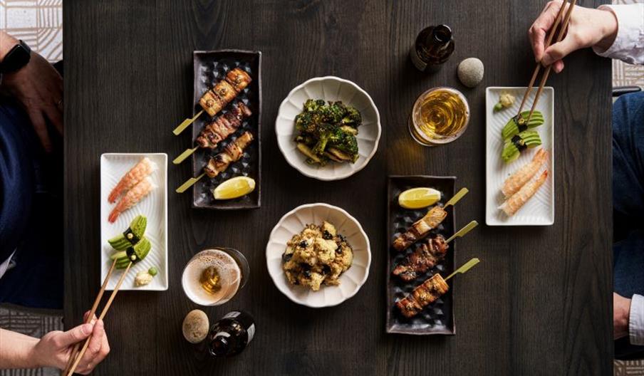 A table layed with sushi, skewers and beer. Two male hands eating.