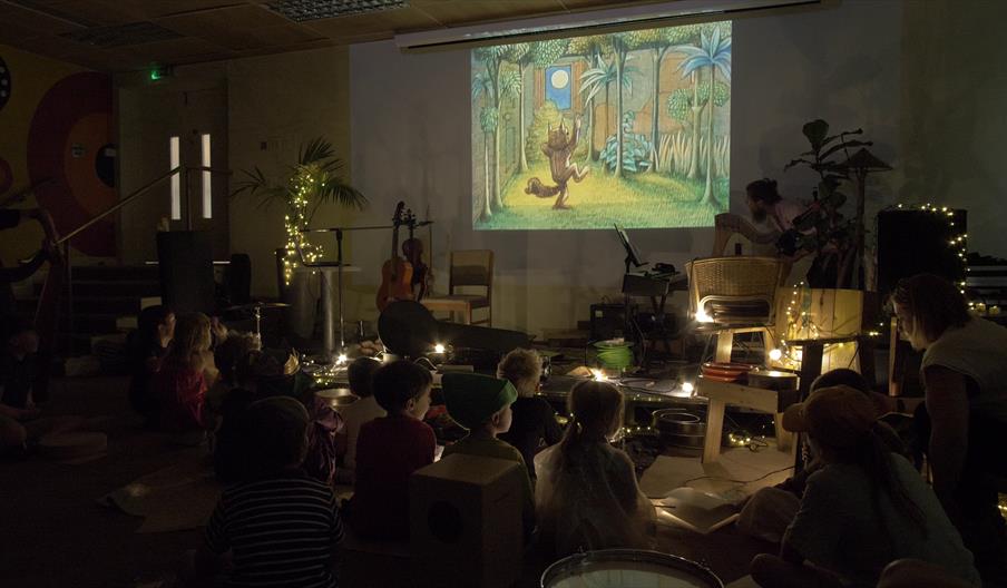 A photograph of young children watching 'Where the Wild Things Are' on a projector screen.
