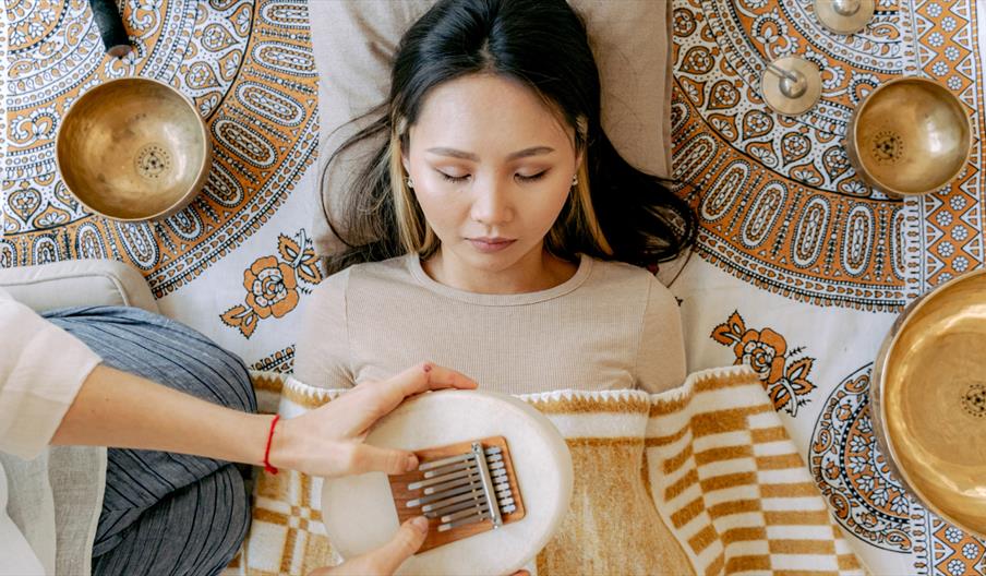 Woman resting during a sound bath surrounded by singing bowls and sound healing instruments.