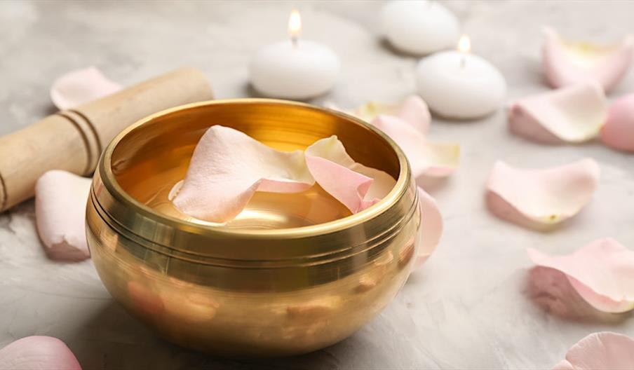 Tibetan sound bowl surrounded by soft flower petals, placed in a serene ritual setting