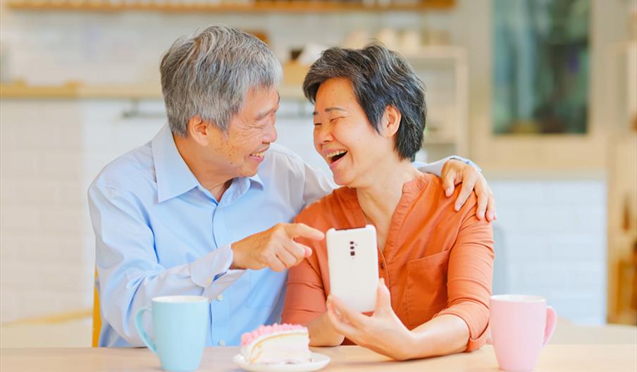 An elderly man and woman pointing at a smartphone and smiling.