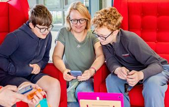 A photograph of two boys and a woman smiling and looking at an tablet screen on a coffee table.
