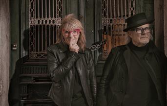 Suzy Starlite & Simon Campbell - man and woman stood in front of an ornate wood green door