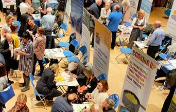 Aerial view of multiple charity stalls at 2023 event in the Theatre space at RHACC with visitors talking to stallholders