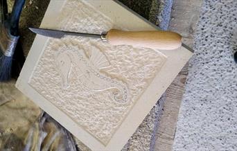 A work in progress image of a slab of stone with a seahorse carved into it