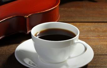 A coffee cup on a wooden table. There is a violin in the background.