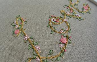 A close-up image of an embroidered cloth that reads 'love', adorned with embroidered flowers