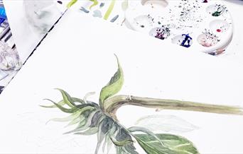Watercolor painting of a sunflower pictured on an open notebook