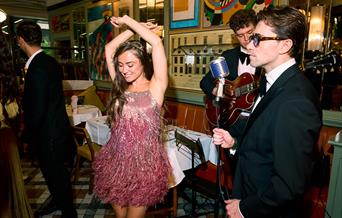 A lady in a pink 1930s style dress dancing to a live performance at The Ivy