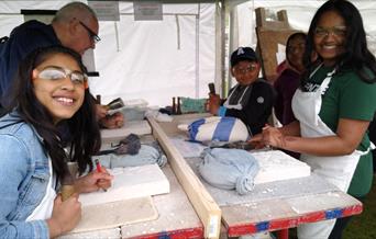An image of five people, two children and three adults, carving into stone inside a tent wearing protective eyewear.