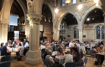 Groups of people sit round tables taking part in a quiz night in a historic church