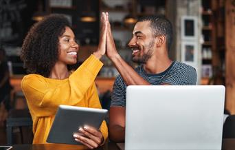 A man and woman high-fiving each other in front of a tablet.