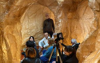 A group of people sitting inside the Templum, which is an immersive installation made out of brown waxed paper.