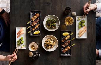 A table layed with sushi, skewers and beer. Two male hands eating.