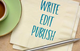 A stock image of a napkin with the words 'Write, Edit, Publish' edited onto it. The napkin is in between a coffee cup and a ballpoint pen.