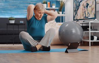 Older person exercising whilst watching a video on a tablet.