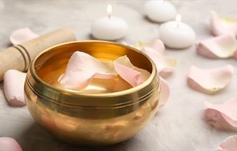 Tibetan sound bowl surrounded by soft flower petals, placed in a serene ritual setting