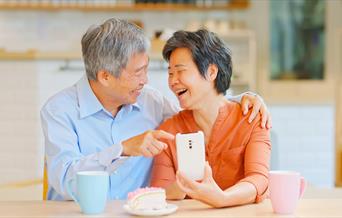 An elderly man and woman pointing at a smartphone and smiling.