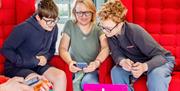 A photograph of two boys and a woman smiling and looking at an tablet screen on a coffee table.