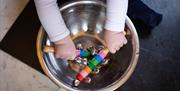 Childs hands holding bells in a metal bowl.