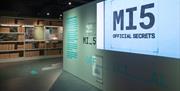 Image of the entrance of the exhibition space. A prominent projection in the gallery exhibits the phrase "MI5: Official Secrets" in large, eye-catchin