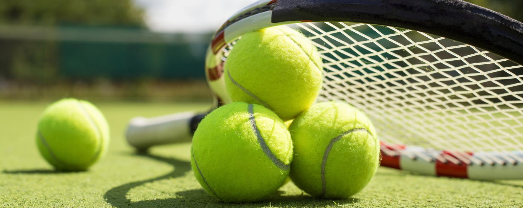 An Image of one tennis racket and four tennis balls on a tennis court