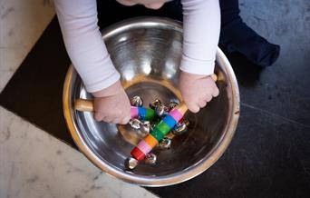 Childs hands holding bells in a metal bowl.