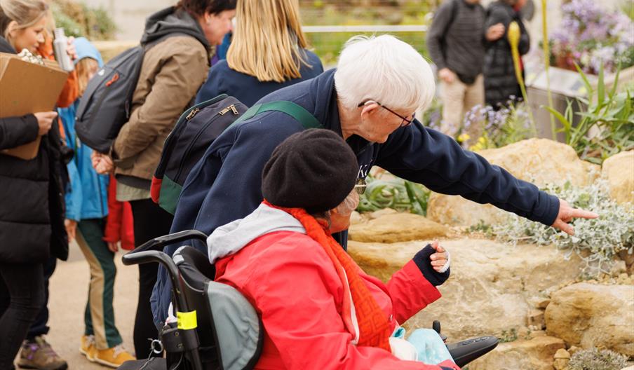 A volunteer guide showing a person in a wheelchair around a rock garden.