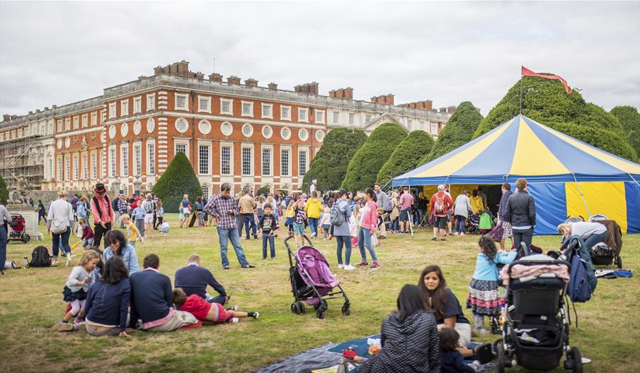Visitors relaxing in the Great Fountain Garden at Hampton Court Palace's Artisan Fayre with a blue and yellow circus tent behind them.