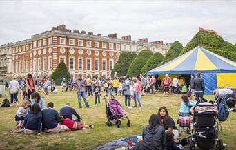 Visitors relaxing in the Great Fountain Garden at Hampton Court Palace's Artisan Fayre with a blue and yellow circus tent behind them.