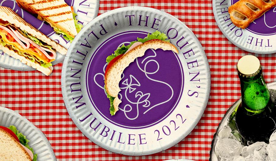 Platinum Jubilee logo on a plate, picnic blanket and half eaten sandwich