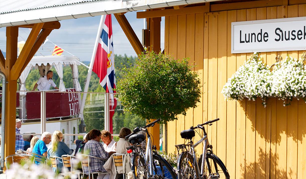 people sitting and eating at Lunde Slusekro while the canal boat MS Henrik Ibsen sails by