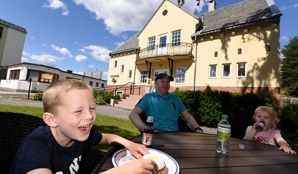 Familie koser seg på uteserveringen til Stasjonen Kafé i hydroparken, i Notodden en sommerdag. Foto