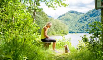 Dame som sitter på en benk med en liten hund foran seg