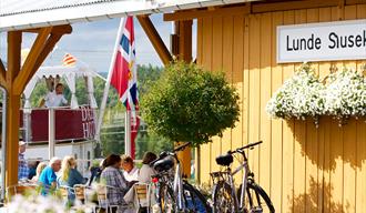 folk som sitter og spiser på Lunde Slusekro mens kanalbåten MS Henrik Ibsen seiler forbi