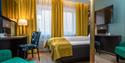 Soverom Thon Hotel Høyers. Gule gardiner, grønn stol, skrivebord, seng med gult teppe.