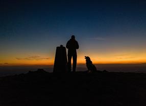 Man and his dog watching the sunrise in The Wrekin