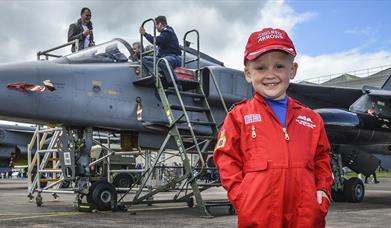 Little boy in red arrows overalls stood in front of an old plane