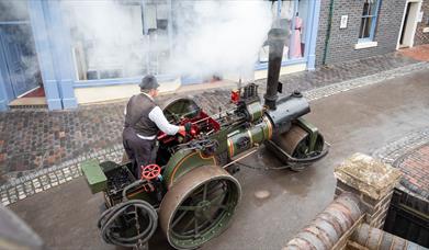 Man on a steam roller driving through Victorian streets.