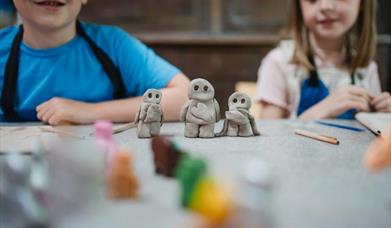 Three small clay figures of people with a boy and girl in the background.
