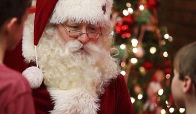 Santa in his red suit, glasses and beard meeting children