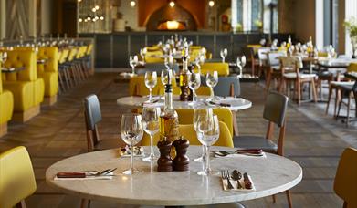 At Wildwood Telford, a modern restaurant with neatly arranged tables set with wine glasses, cutlery, and condiments, yellow chairs add to the cozy atm