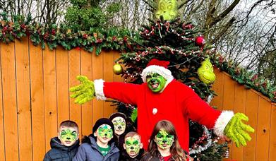 The Grinch with children in Grinch face paint in front of a Grinch Christmas tree.