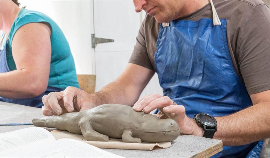 A man in a blue apron building with clay